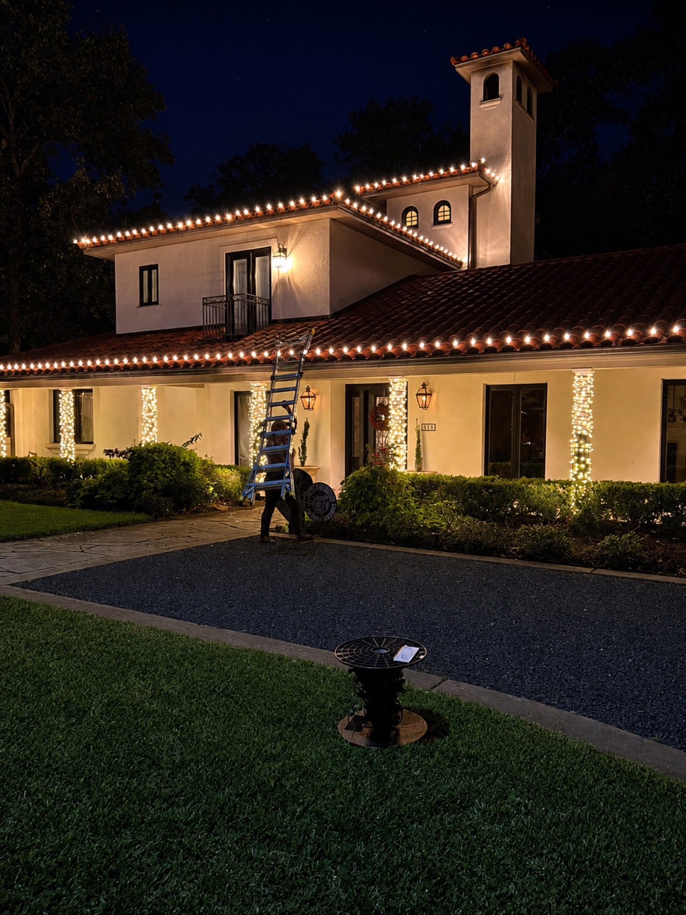 Professional installer carrying a ladder at a home decorated with Christmas lights.