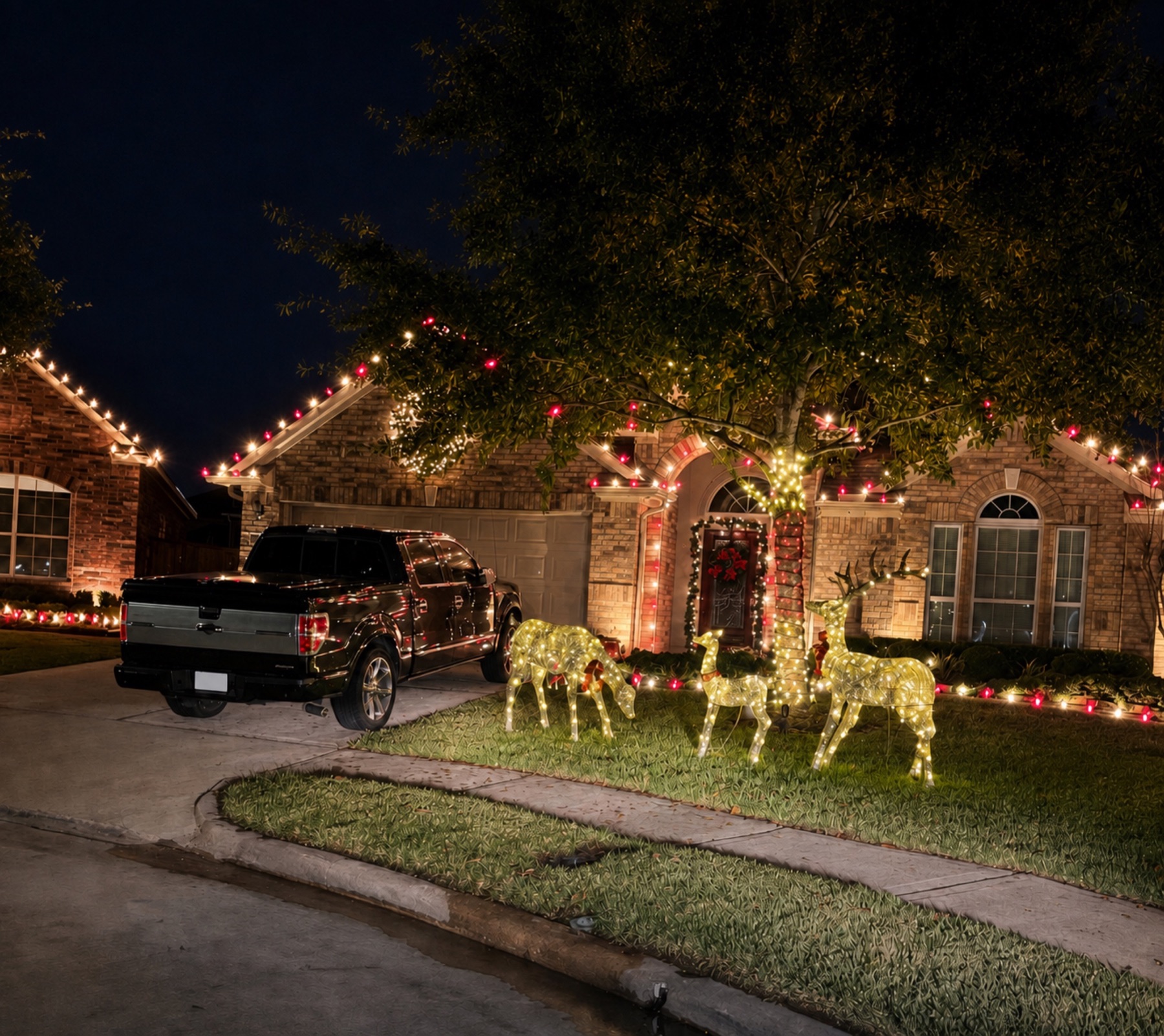 Brick home decorated with alternating red and warm white roofline lights, a wrapped tree, and glowing reindeer.